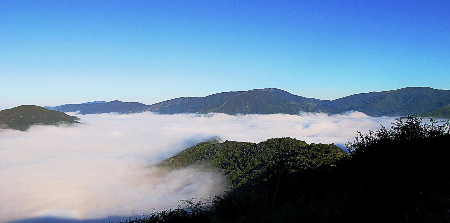 Cloud filling a valley in the Serra do Courel at dawn, with wooded ridges rising above it.